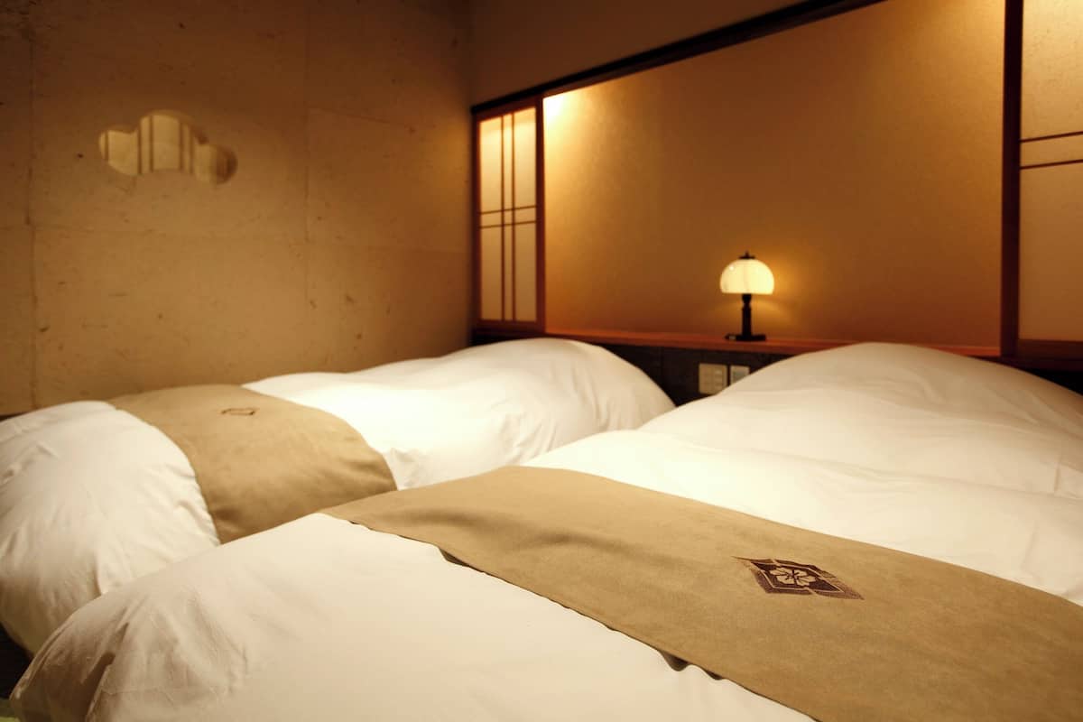 Une chambre d’hôtel avec deux lits, une table de chevet avec une lampe et un mur orné d’un panneau décoratif.