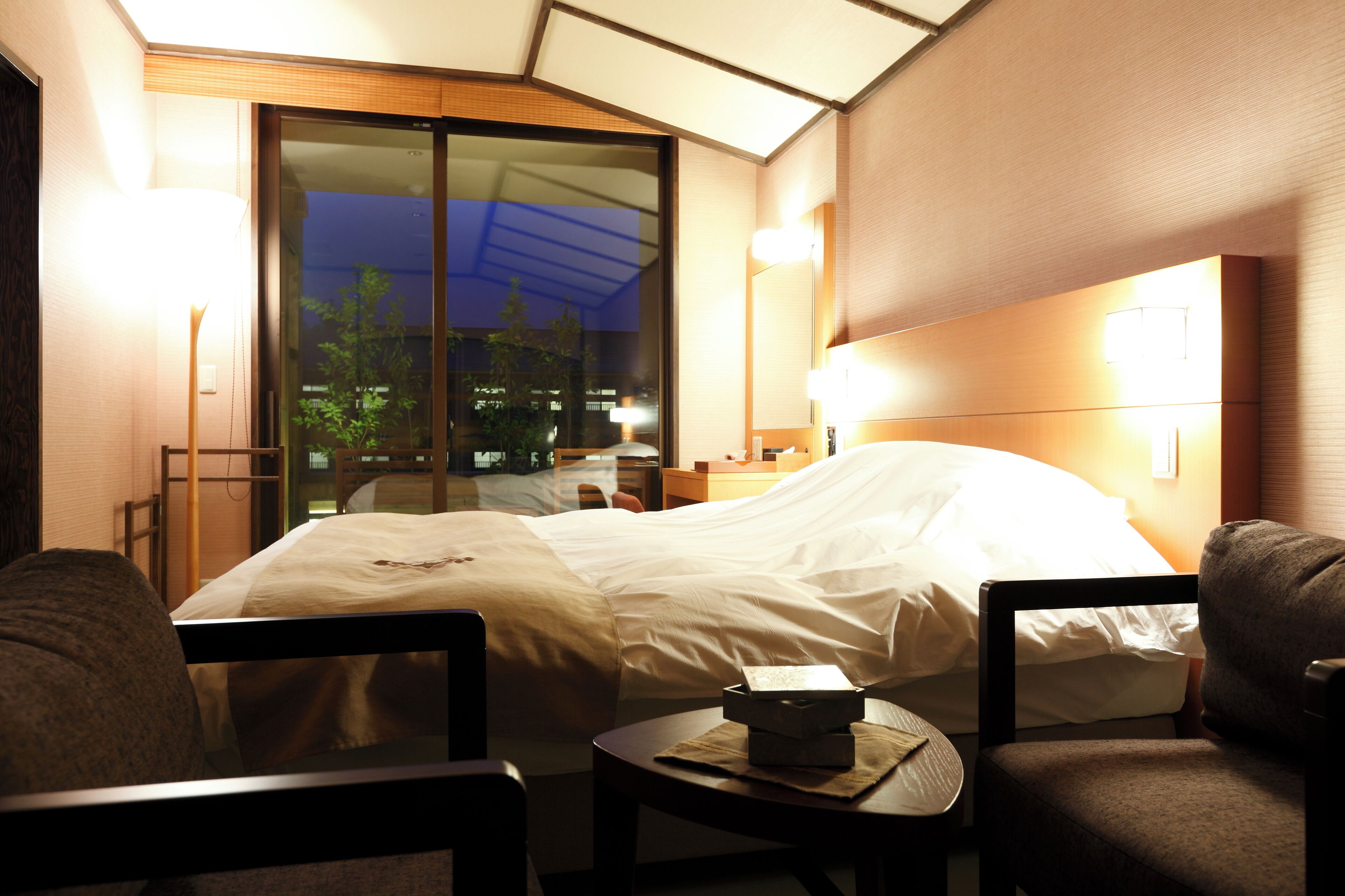 A hotel room with a bed, two chairs, a small table, and a nightstand.