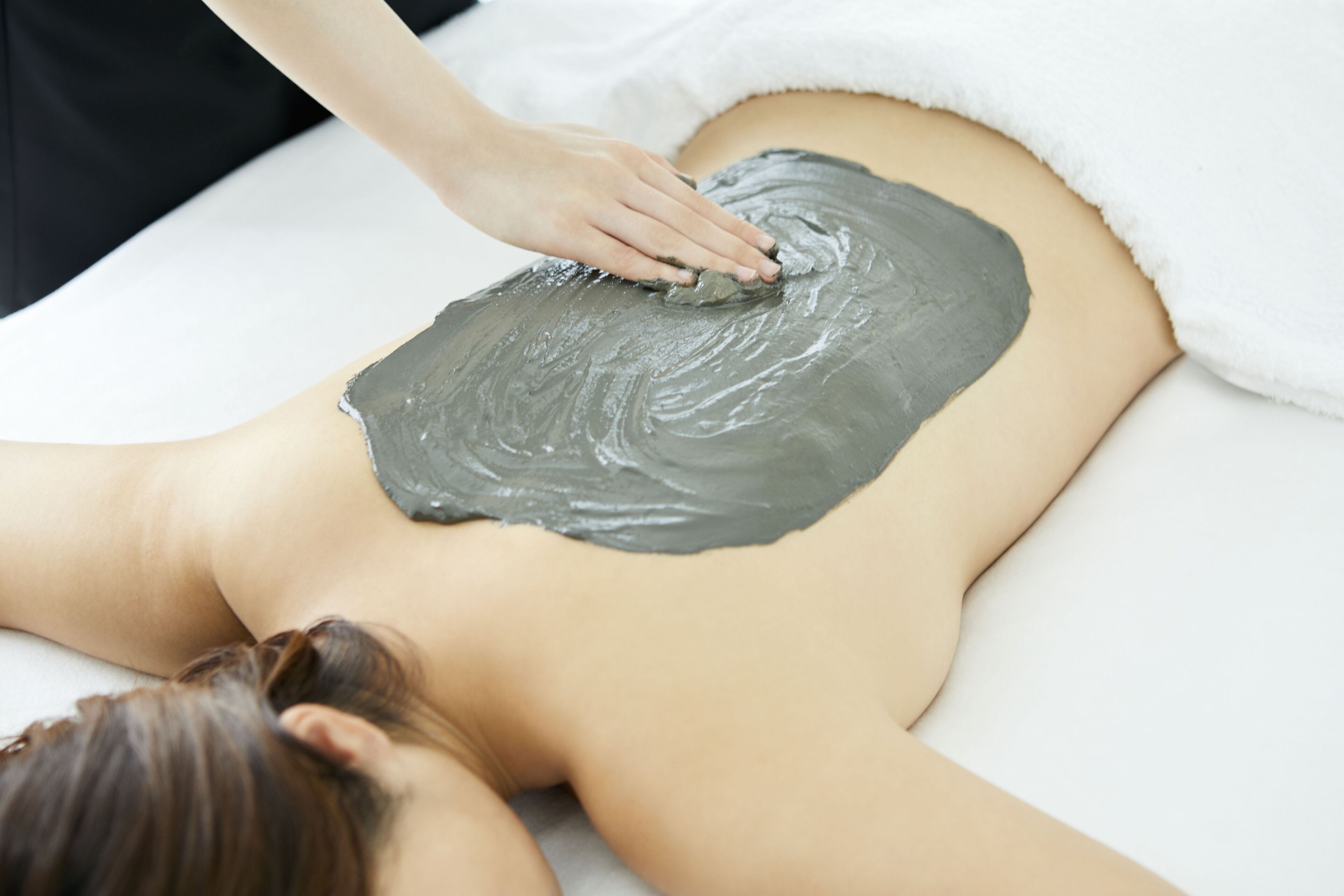 A person receiving a body treatment with a grey substance on their back.