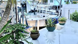 A marina with boats docked, a palm tree, and potted plants on a reflective surface. - Beautiful Waterfront Villa (Tavernier)