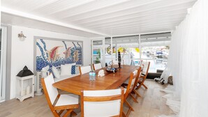 A dining area with a wooden table, white chairs, a mosaic wall art, and a view of the sea through large windows. - Beautiful Waterfront Villa (Tavernier)