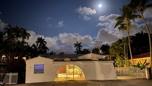 A white building with a curved entrance, palm trees, and a clear night sky with the moon. - 3Bd. & 2Bth. Private Island Security Gated Villa Miami Beach (North Bay Village)