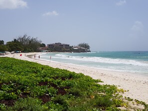 Ein Strand mit einem Hotel im Hintergrund, sandigem Ufer und grüner Vegetation im Vordergrund.
