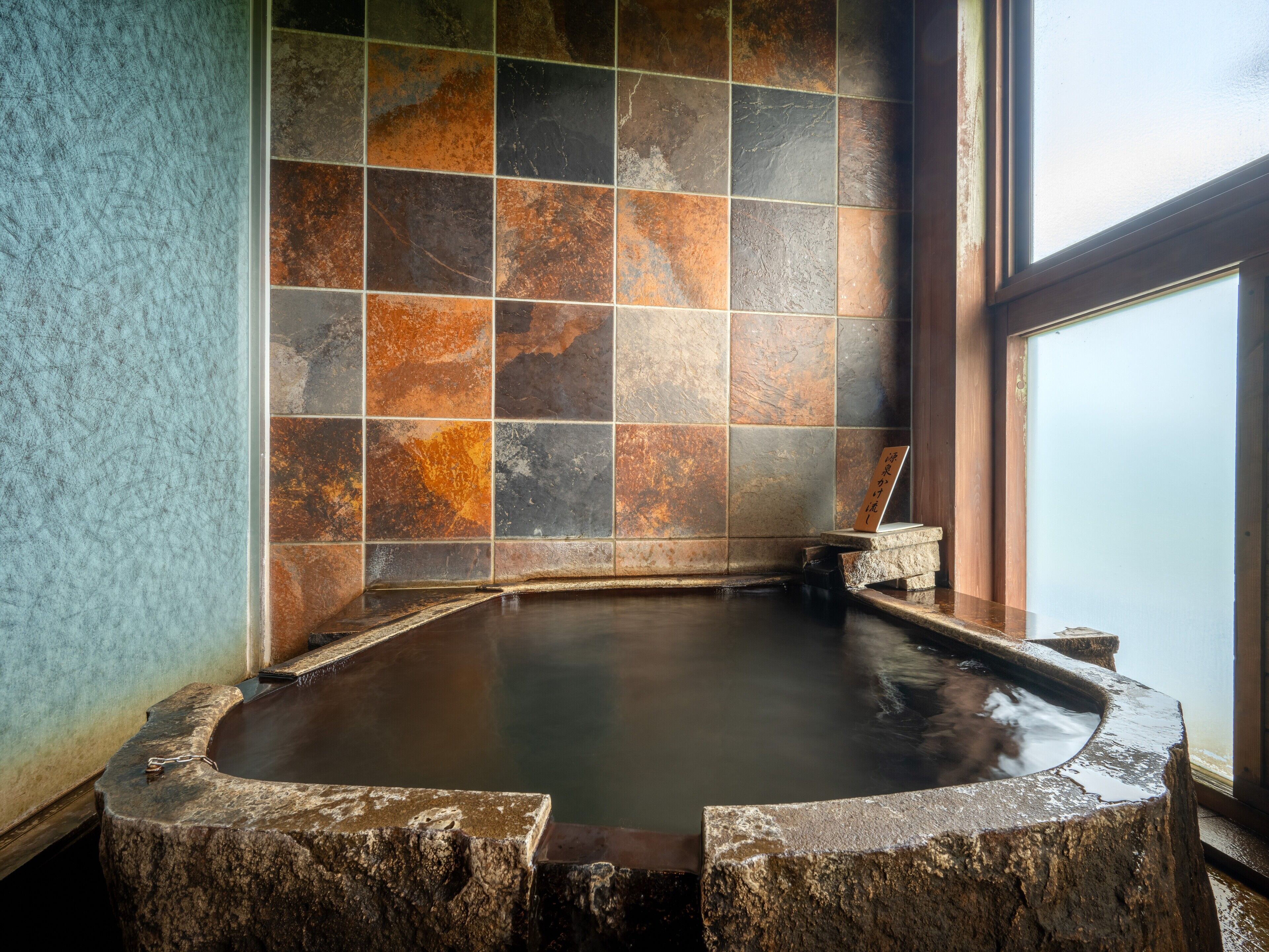 A stone hot tub with a tiled wall in the background.