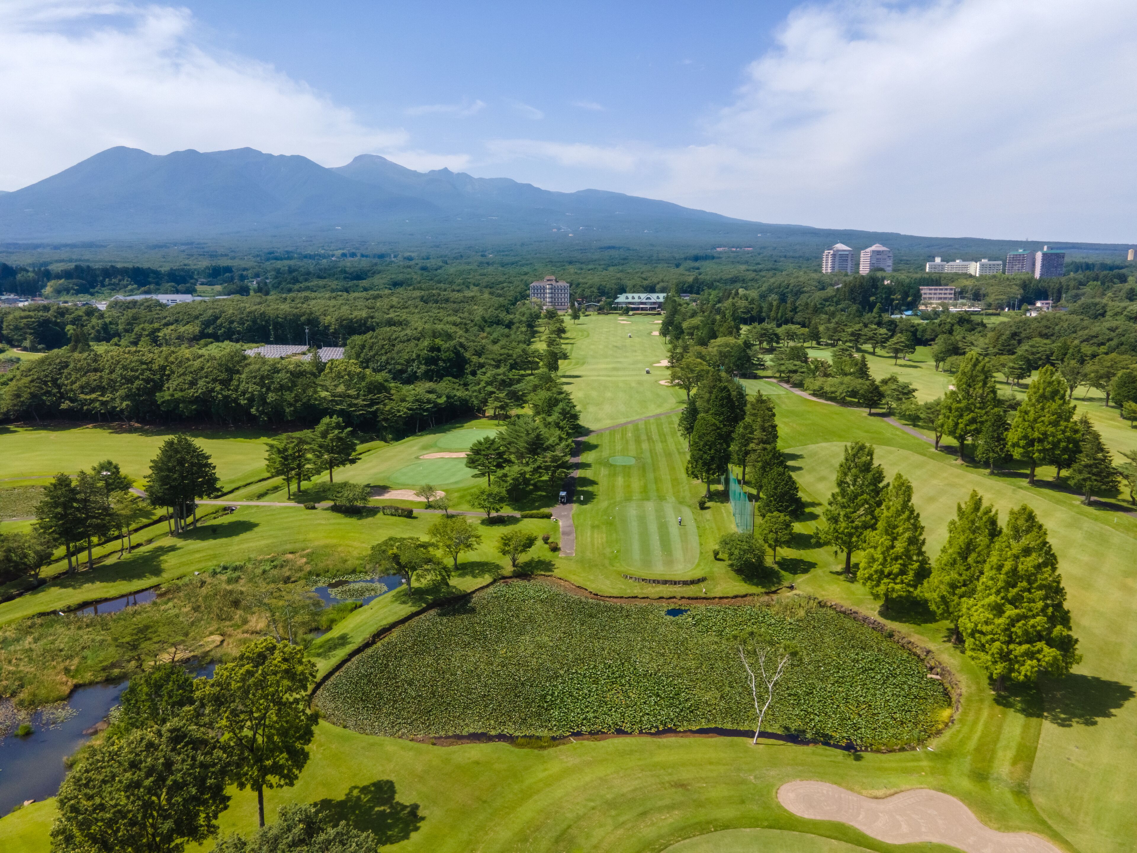 A golf course with a pond, trees, and buildings in the background.
