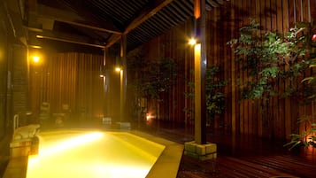 A hot tub area with wooden walls and a tiled floor, surrounded by potted plants.