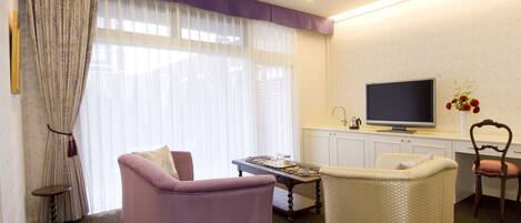 A living room with a purple sofa, a wicker chair, a small table, and a television on a cabinet.