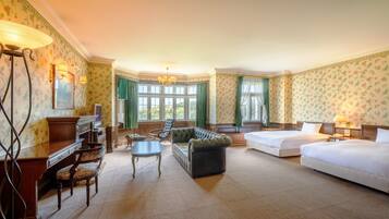 A hotel room with a sofa, a bed, a desk, and a chair. There are windows with curtains and a chandelier.