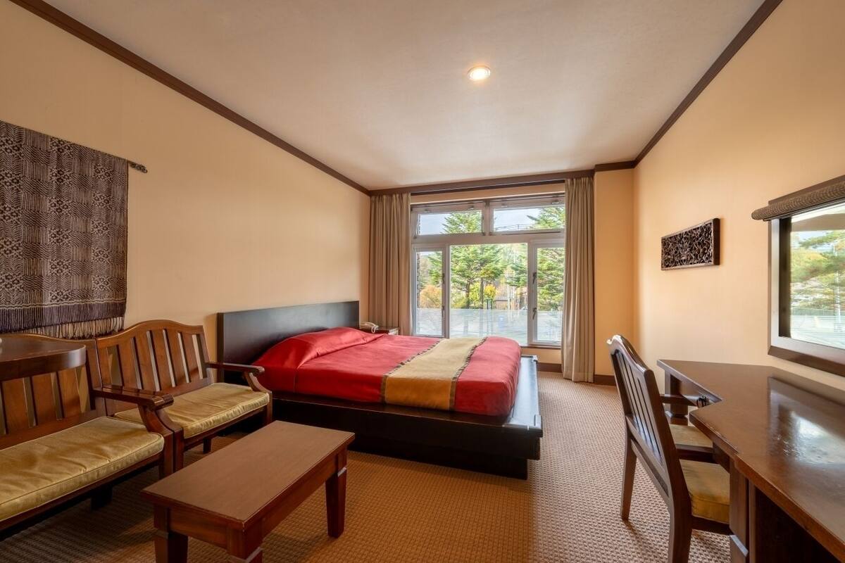 A hotel room with a bed, two chairs, a small table, and a window with a view of trees.