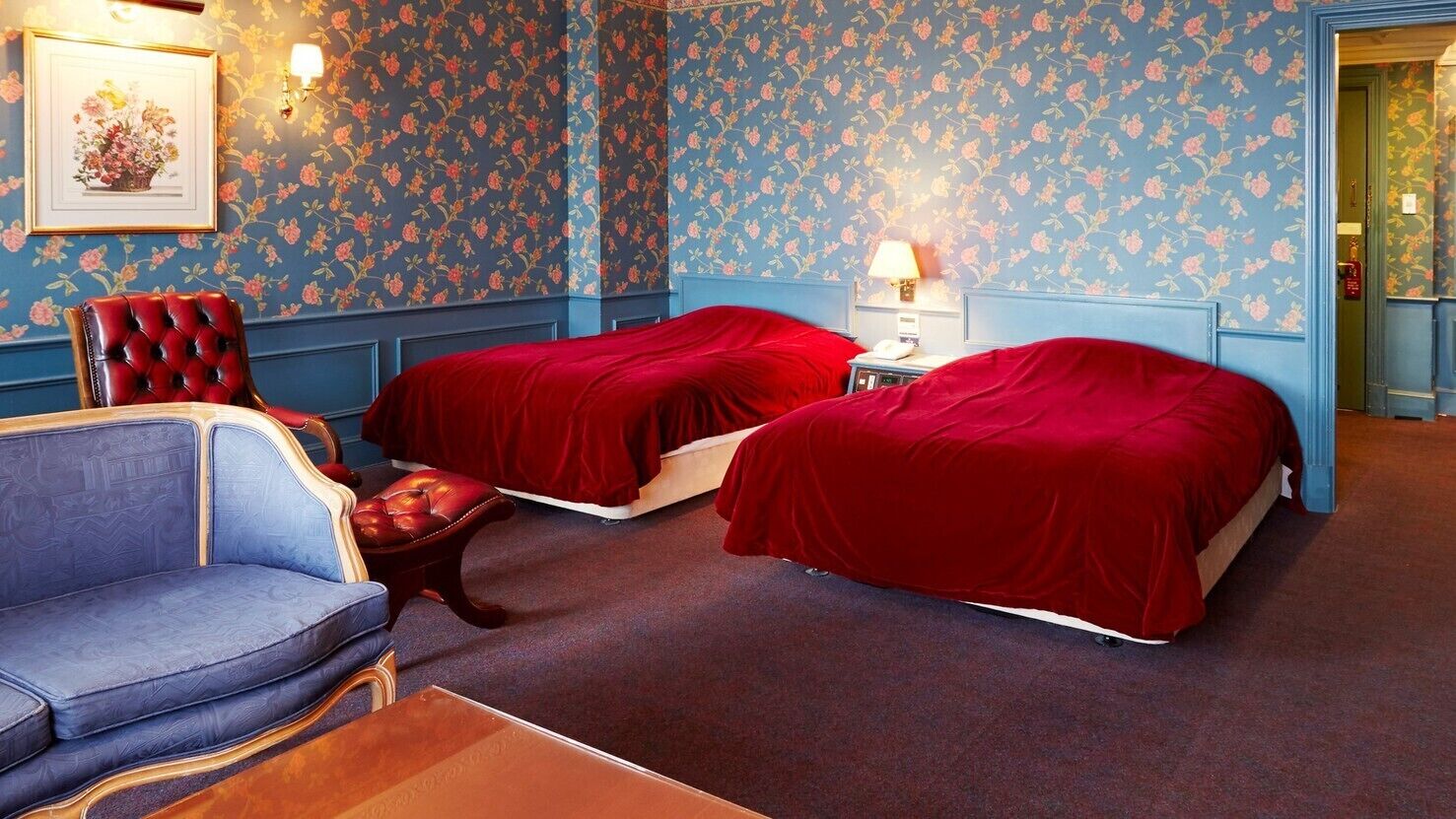 Una habitación con dos camas, un sofá, una silla y una mesita de noche con lámpara.