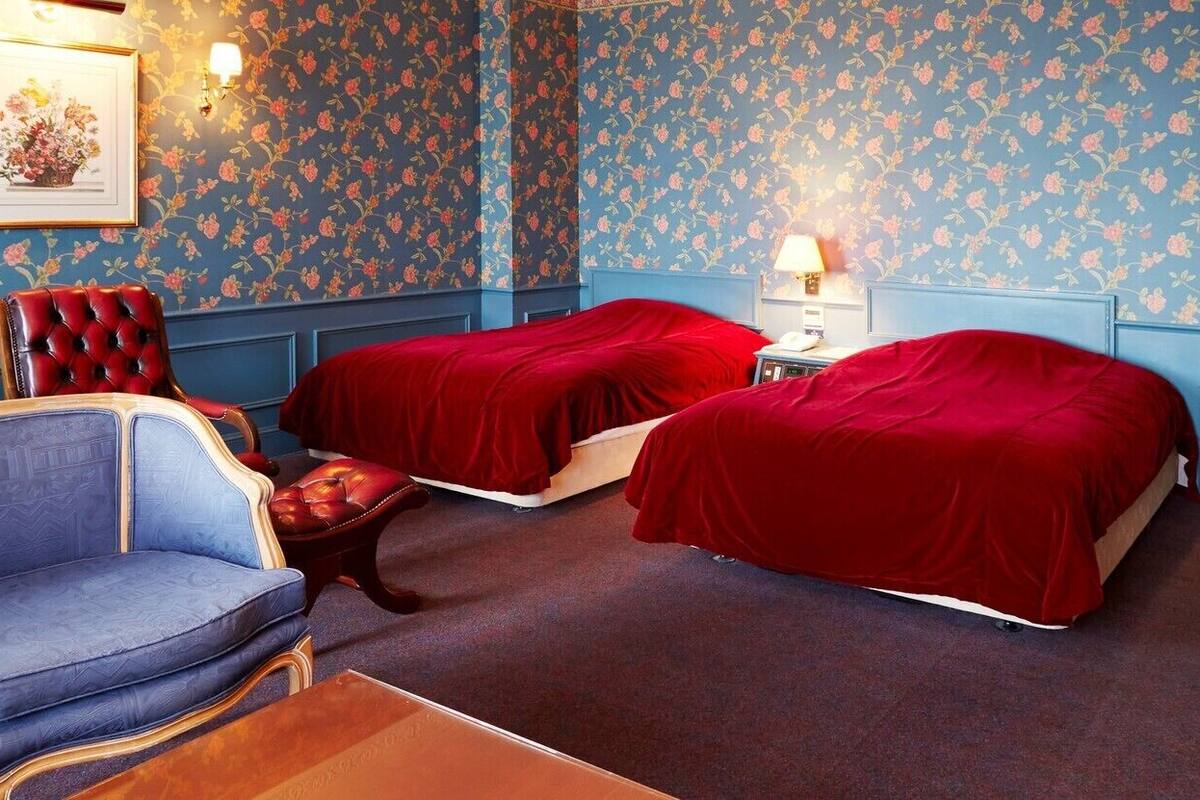 A room with two beds, a sofa, a chair, and a nightstand with a lamp.