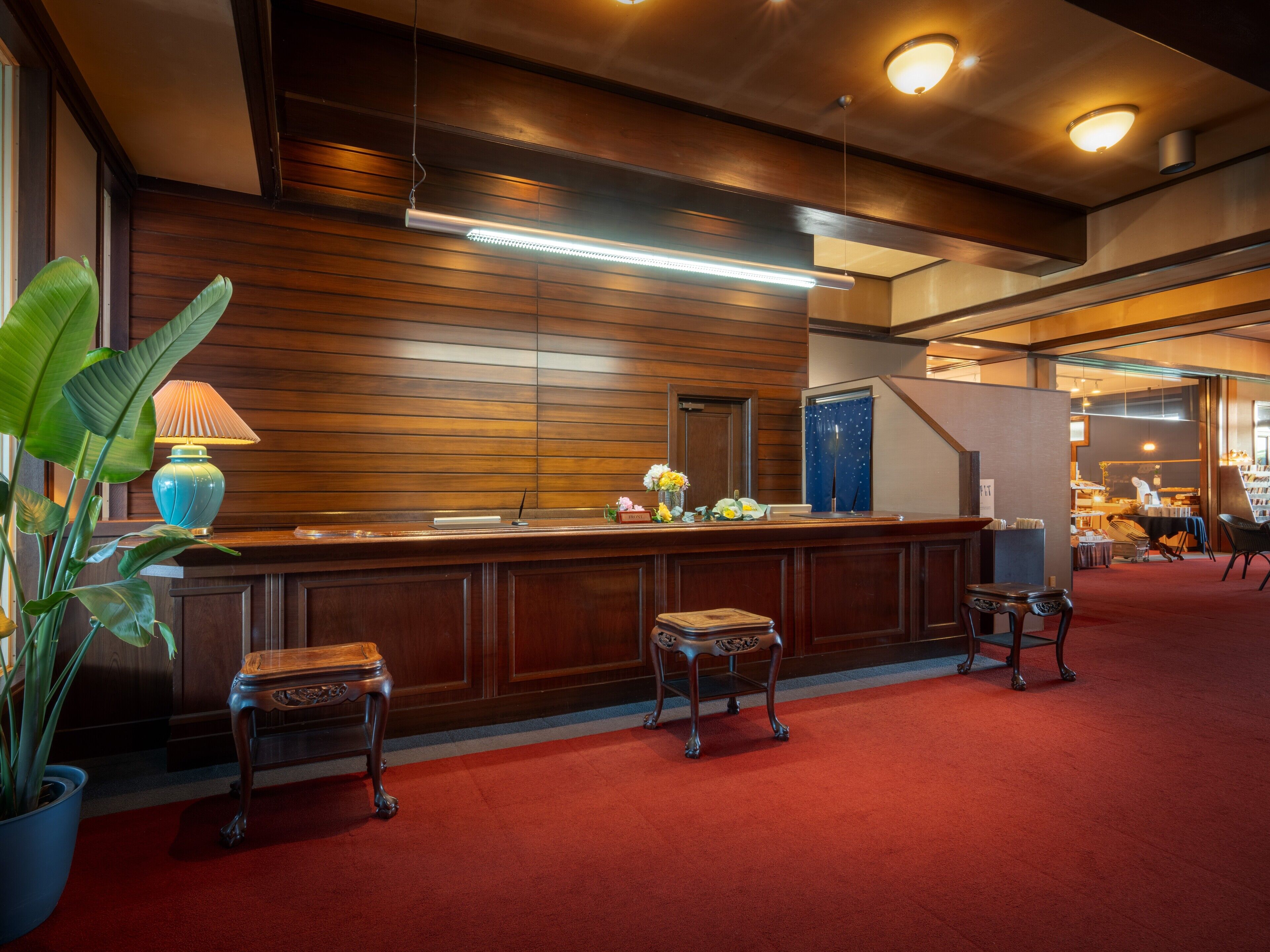 A reception area with a wooden reception desk, a blue lamp, a potted plant, and a red carpet.