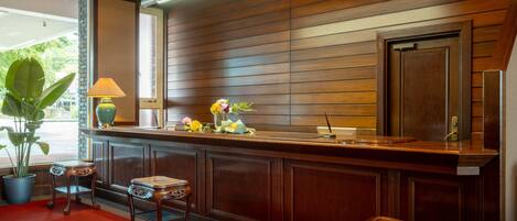 A reception area with a wooden counter, a lamp, a vase with flowers, and a potted plant.