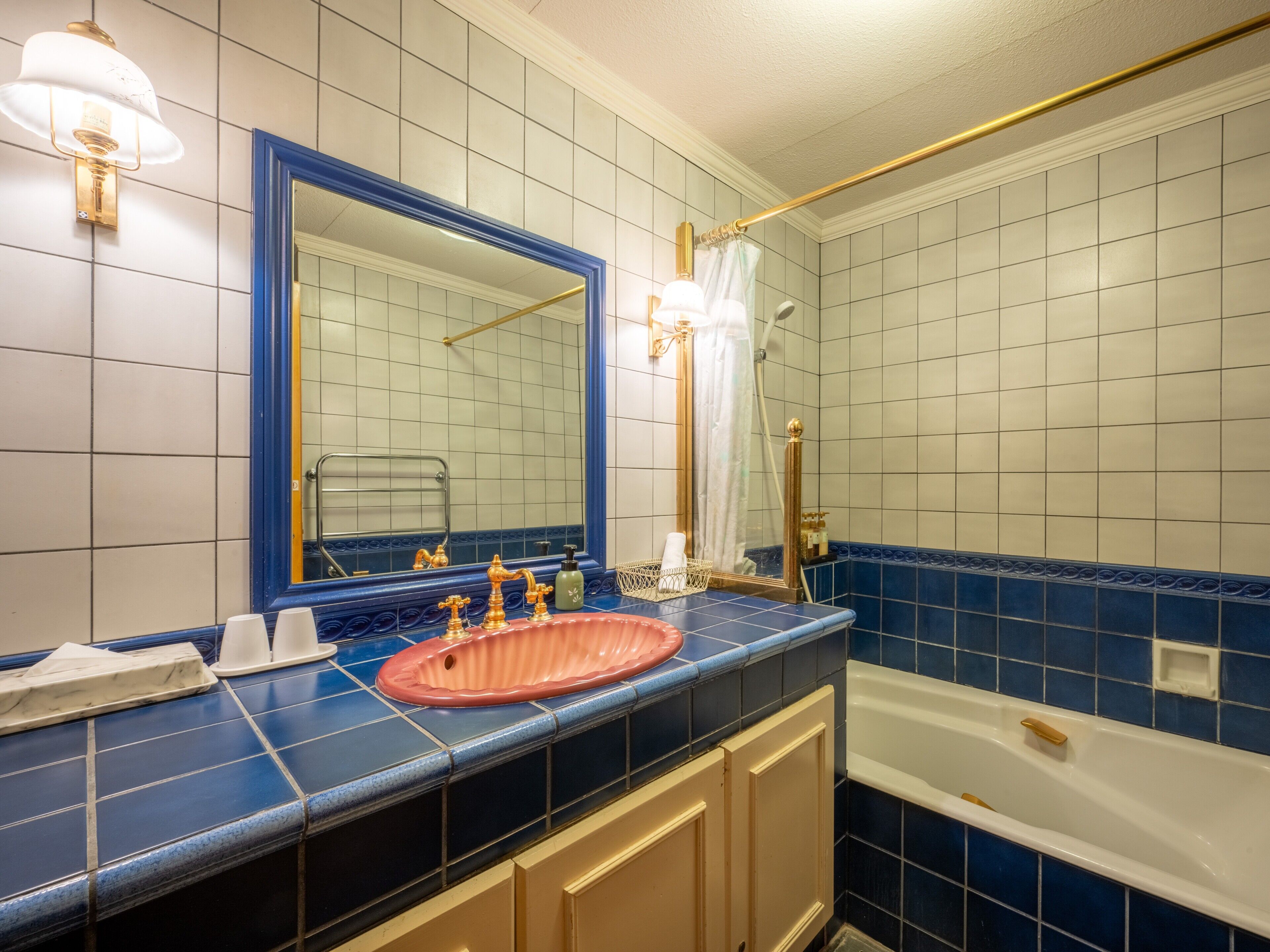 A bathroom with a blue-tiled wall, a large mirror, a sink with gold faucets, and a bathtub.