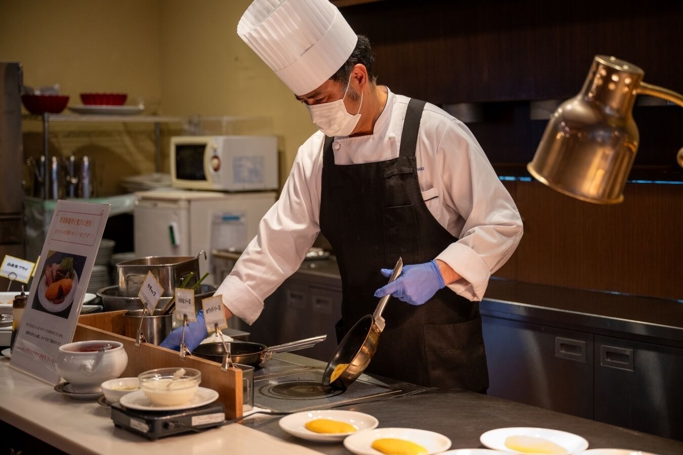 Uno chef in una cucina professionale, con cappello bianco e grembiule nero, sta preparando del cibo.