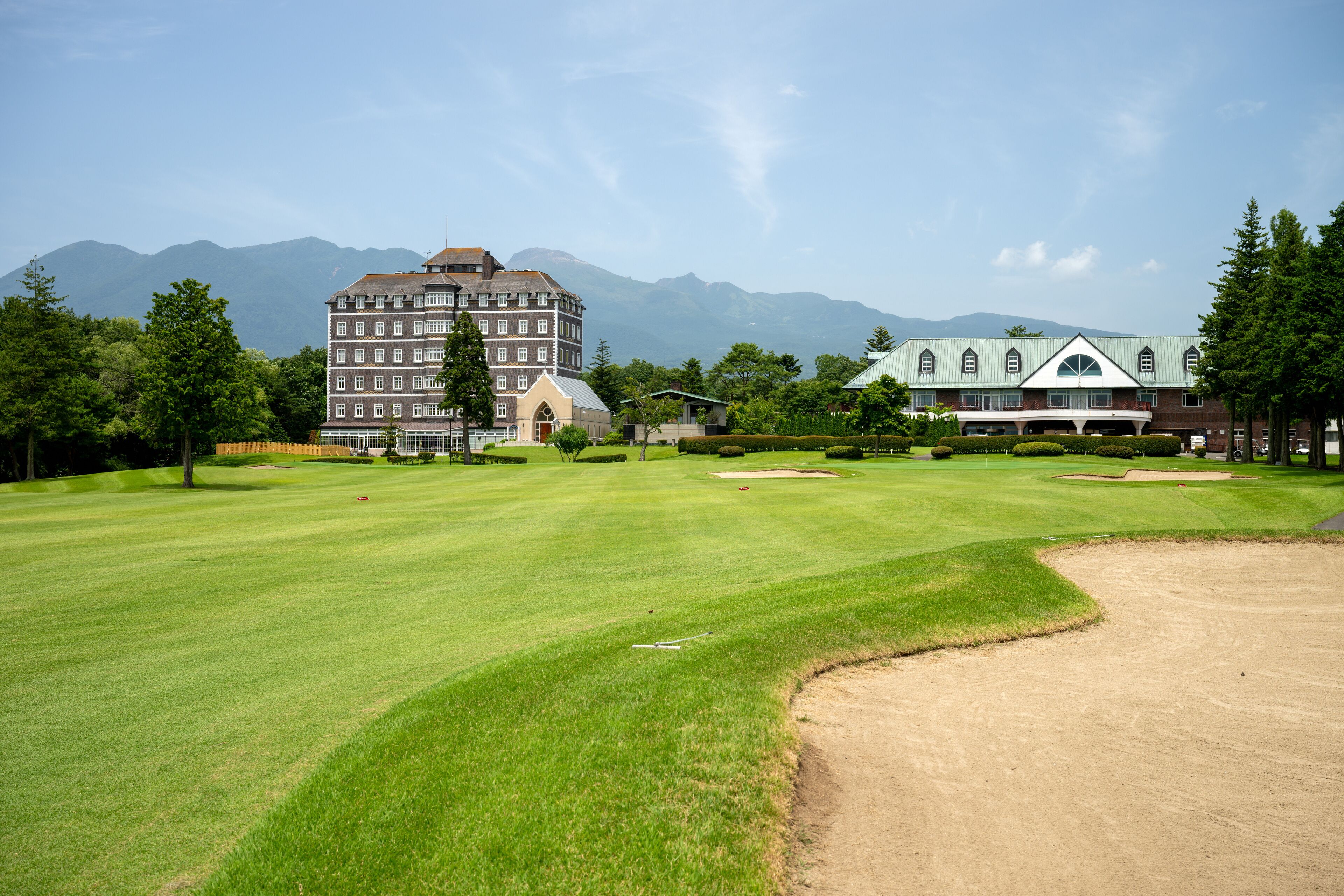 A golf course with a large building in the background, surrounded by trees and mountains.