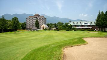 A golf course with a large building in the background, surrounded by trees and mountains.
