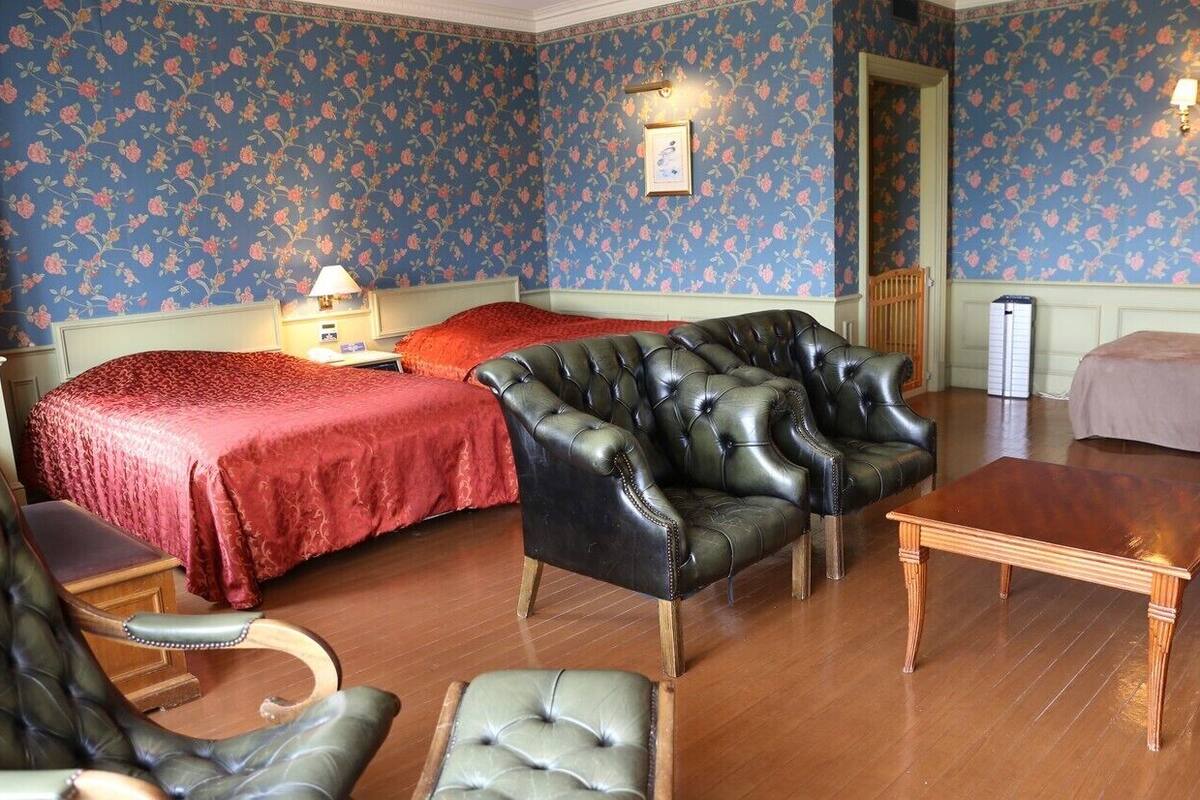 A room with two beds, a leather armchair, a wooden coffee table, and a patterned wallpaper.
