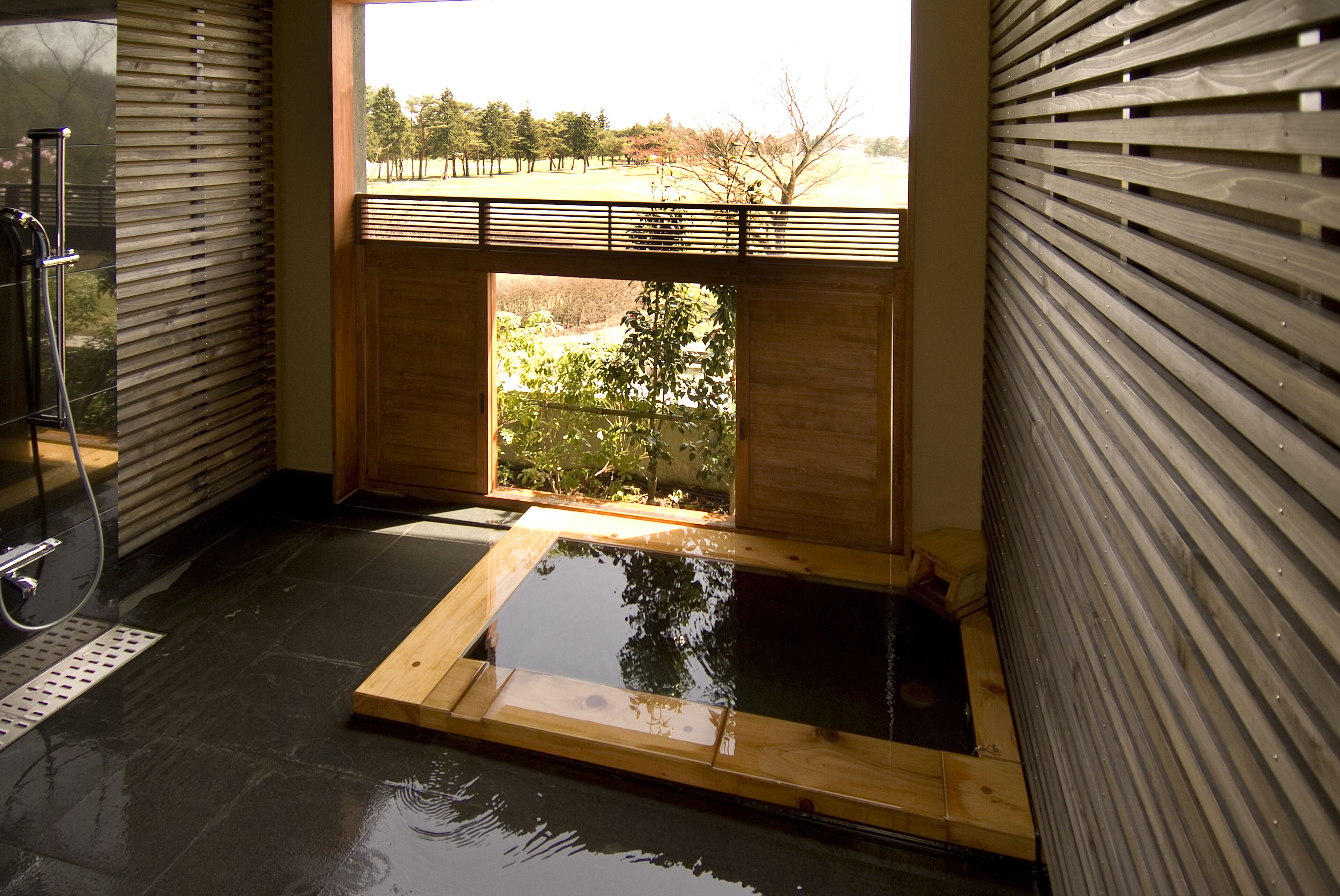 A modern spa room with a wooden floor, a glass-enclosed hot tub, and a view of a garden.