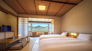 Quarto de hotel com uma cama grande, uma escrivaninha, uma televisão e vista para montanhas.
