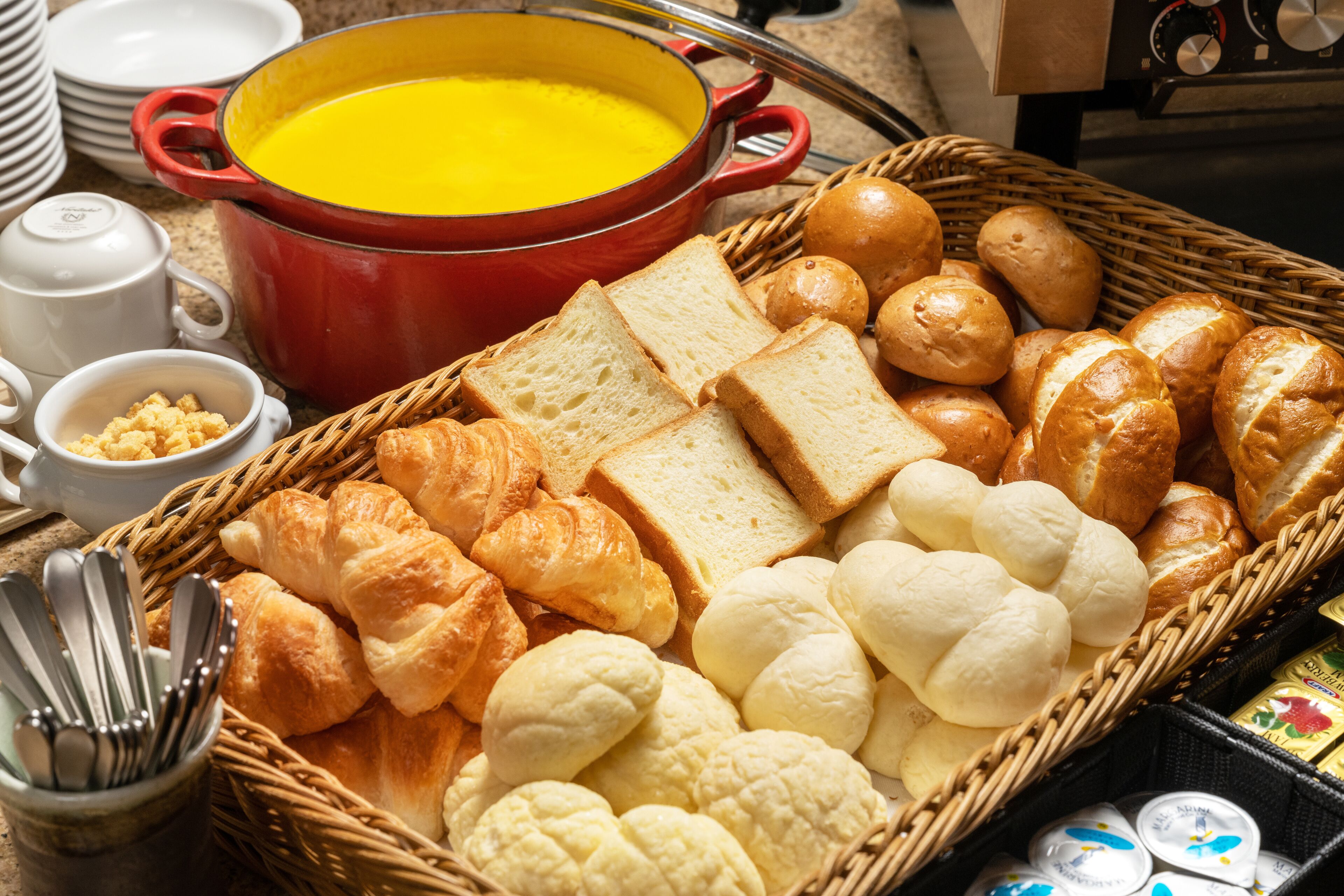 A breakfast setting with bread, croissants, and a pot of soup.