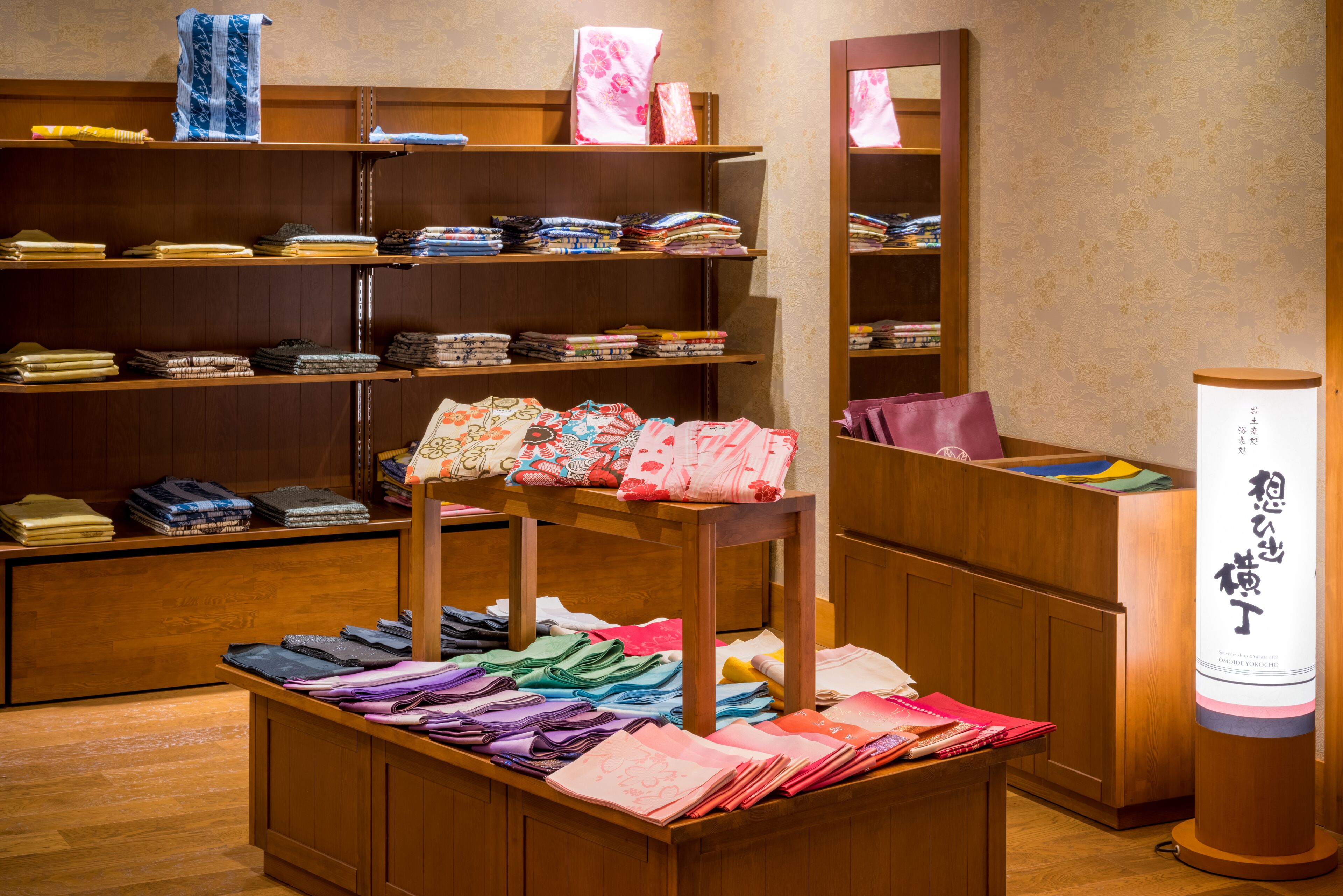 Una tienda ordenada con estantes llenos de textiles doblados y una mesa exhibidora con distintos tipos de telas.