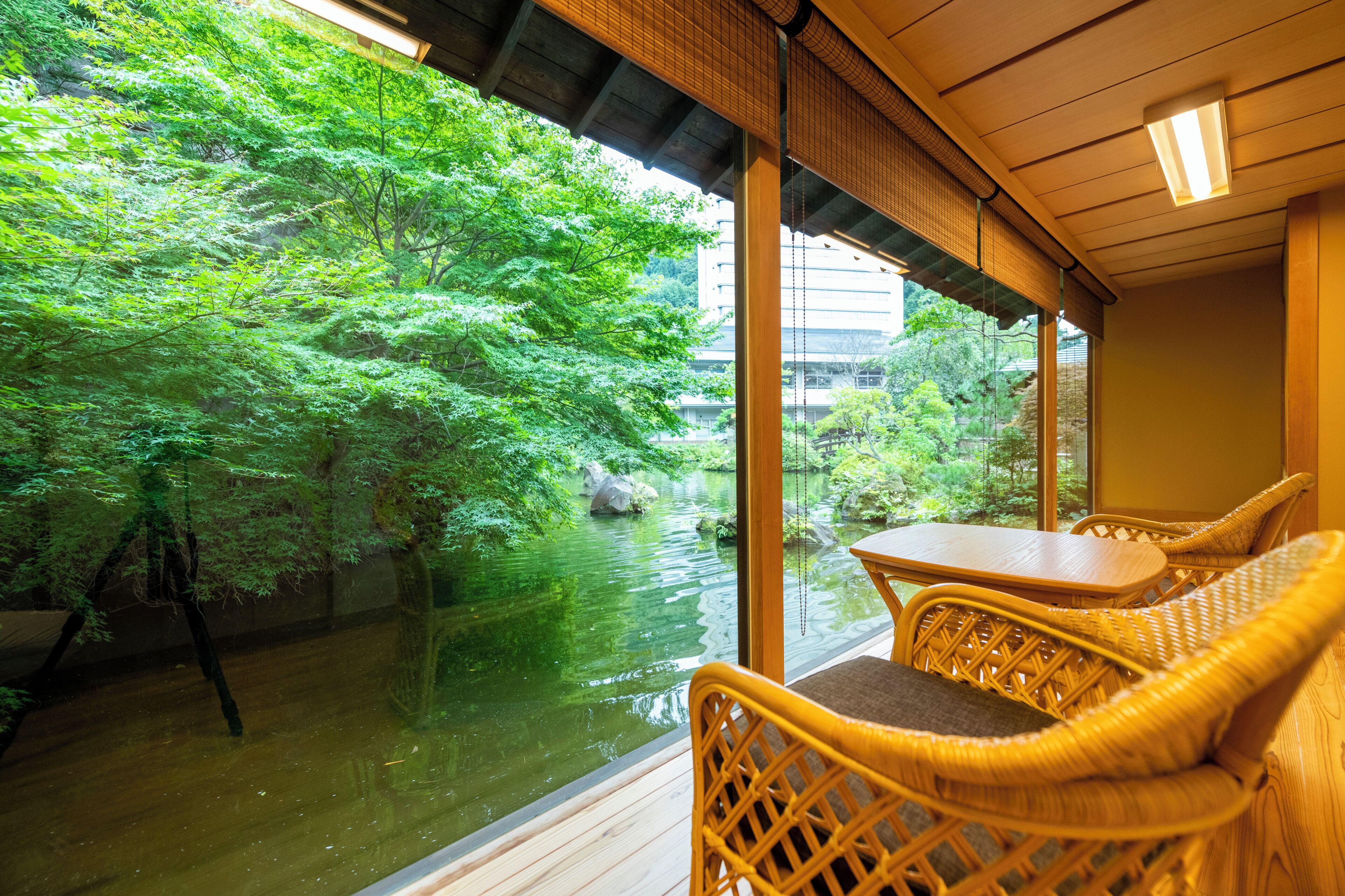 A room with a view of a water body and greenery, wicker furniture, and a wooden ceiling.