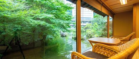 A room with a view of a water body and greenery, wicker furniture, and a wooden ceiling.