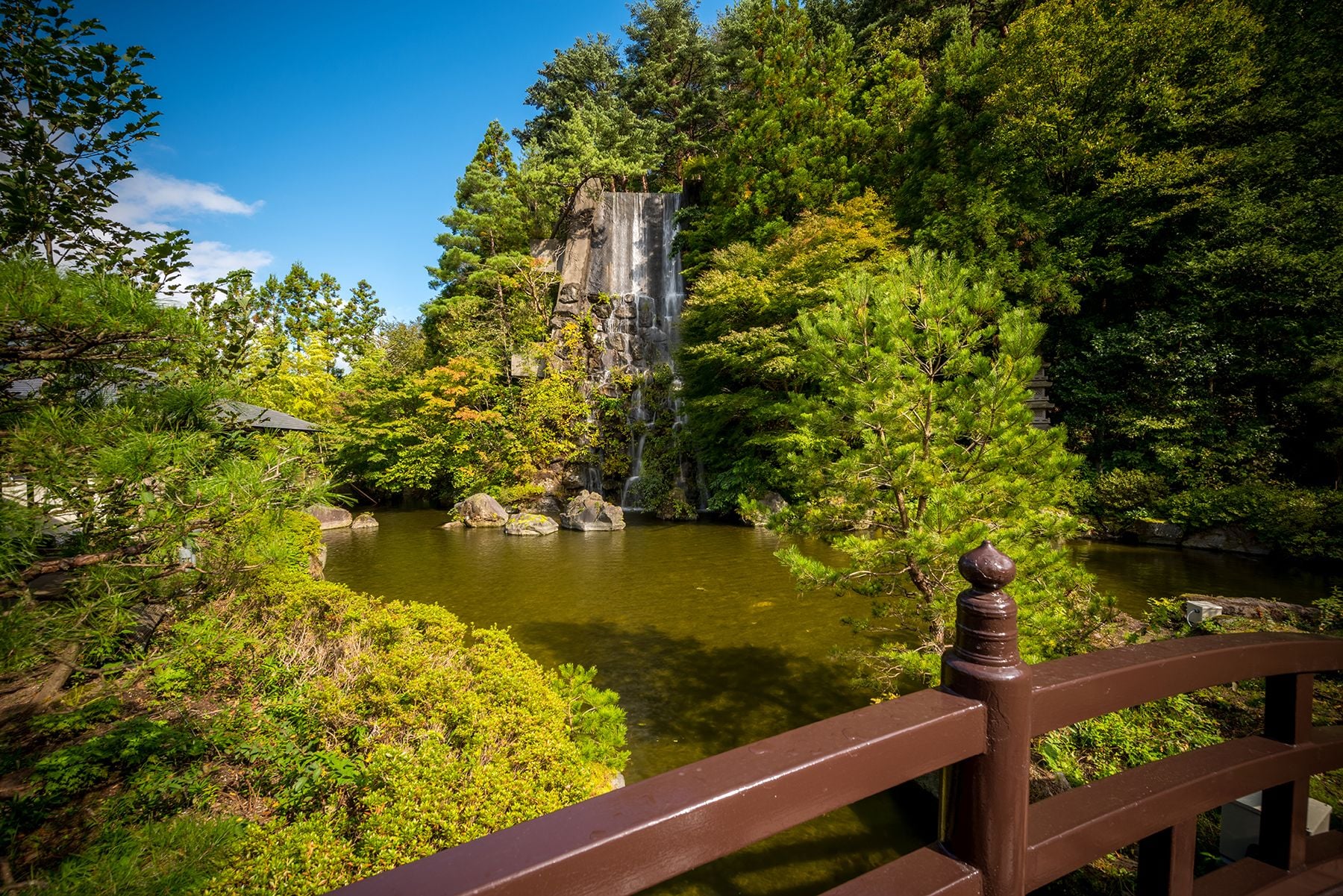 Een rustgevende tuin met een waterval, weelderige begroeiing en een houten brug.