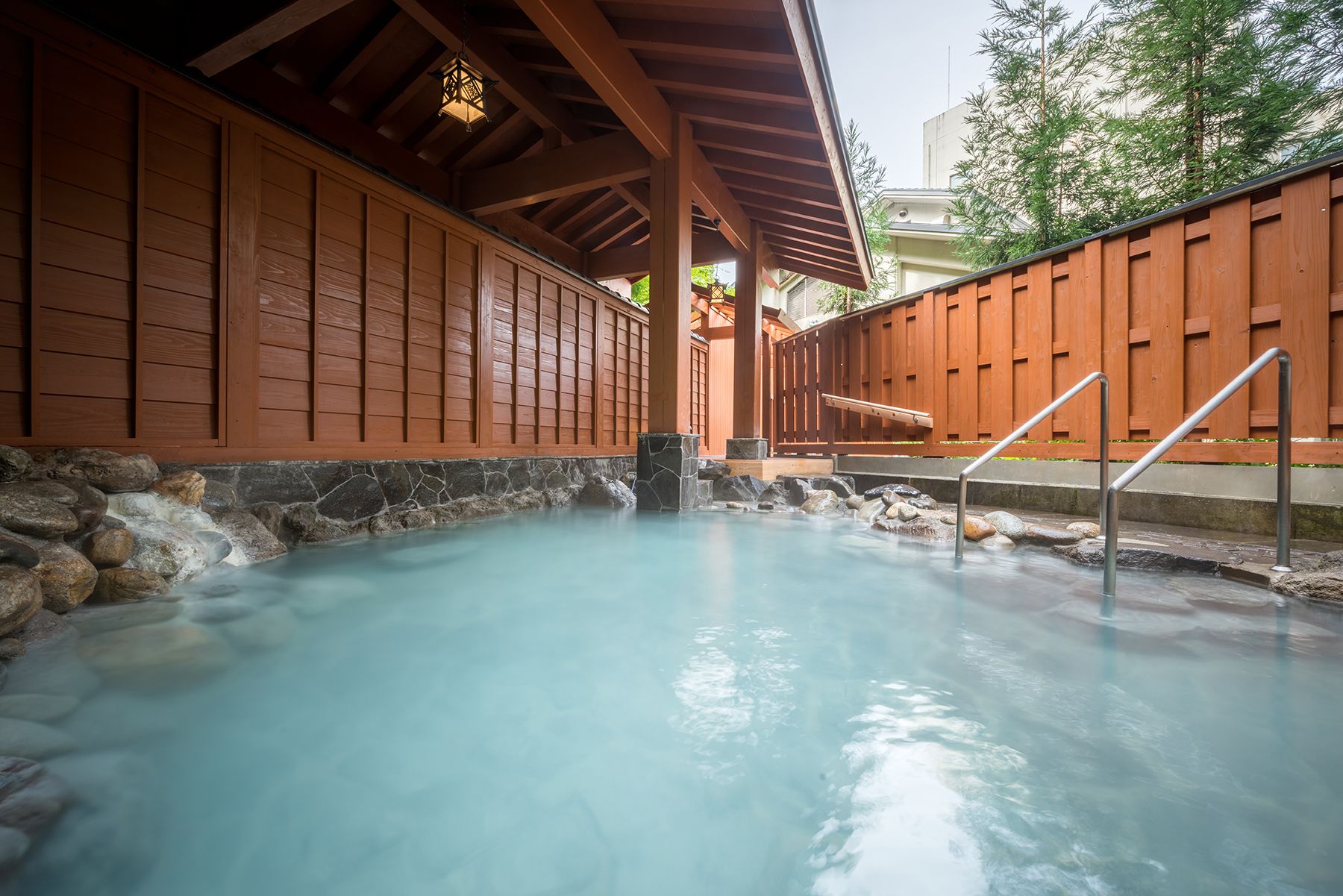 Un onsen japonés tradicional con estructura de madera, paredes de piedra y una fuente termal cristalina.