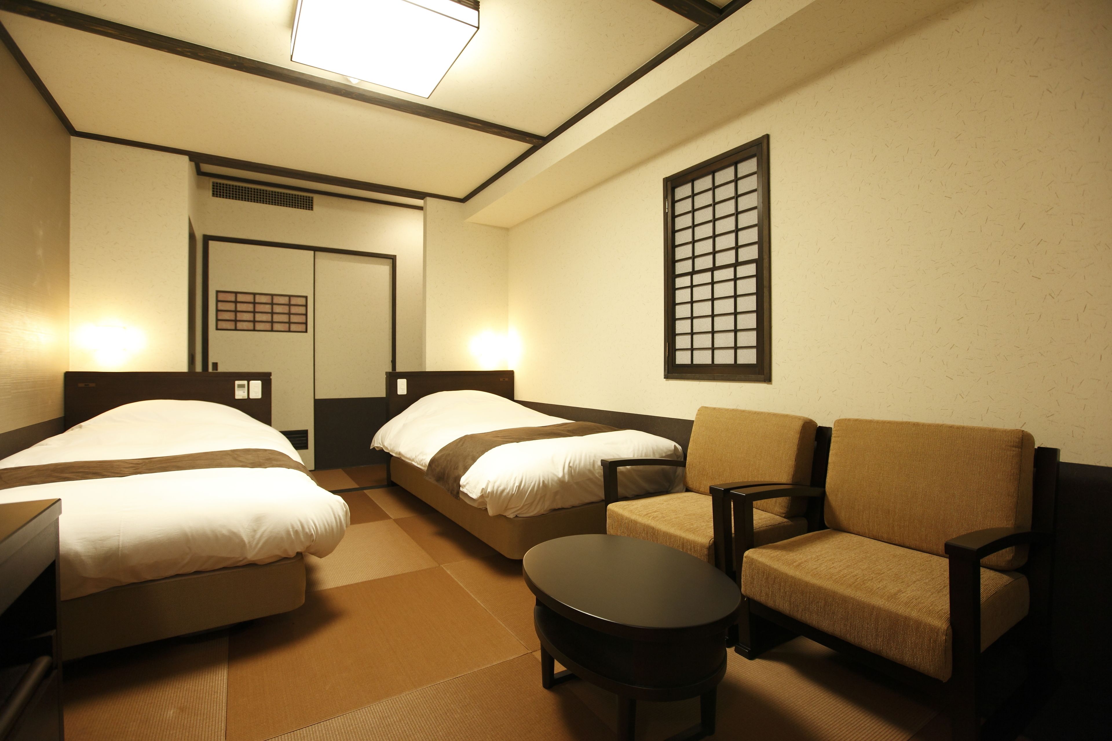A hotel room with two beds, a sofa, a small table, and a traditional Japanese shoji screen.