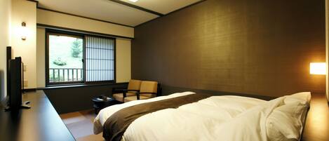 A hotel room with a bed, a TV, a chair, and a window with blinds.