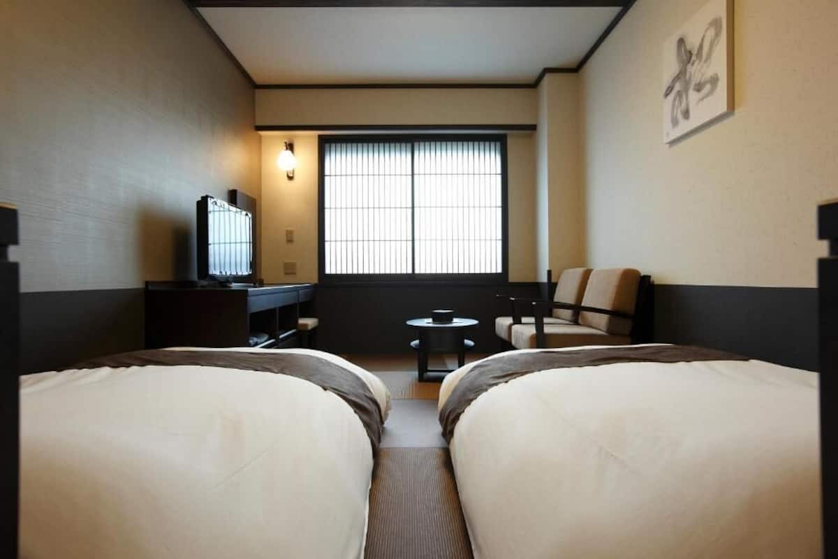 A hotel room with two beds, a desk, a chair, a television, and a window with blinds.