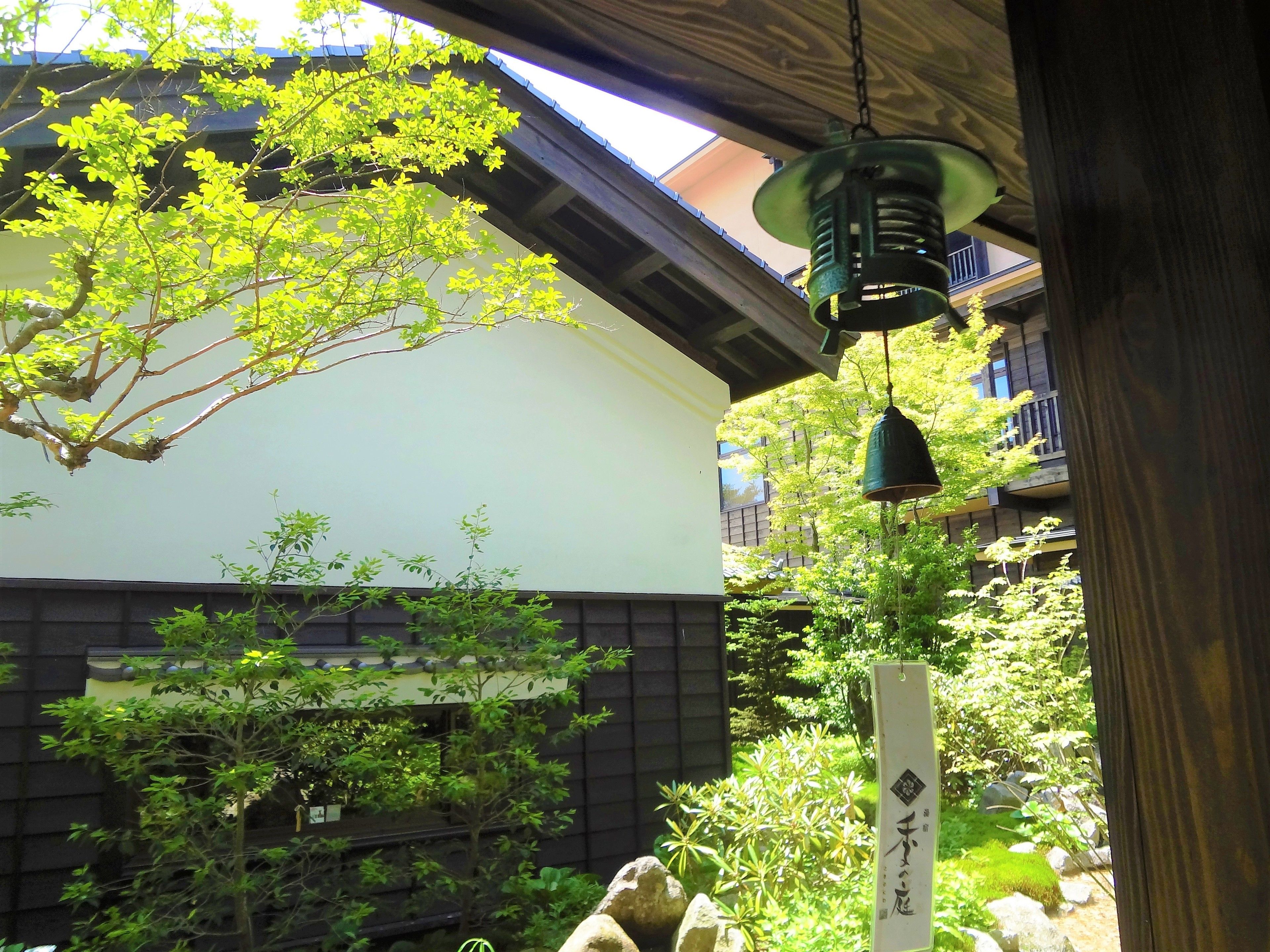 A traditional Japanese garden with a wooden structure, a hanging lantern, and a stone path.