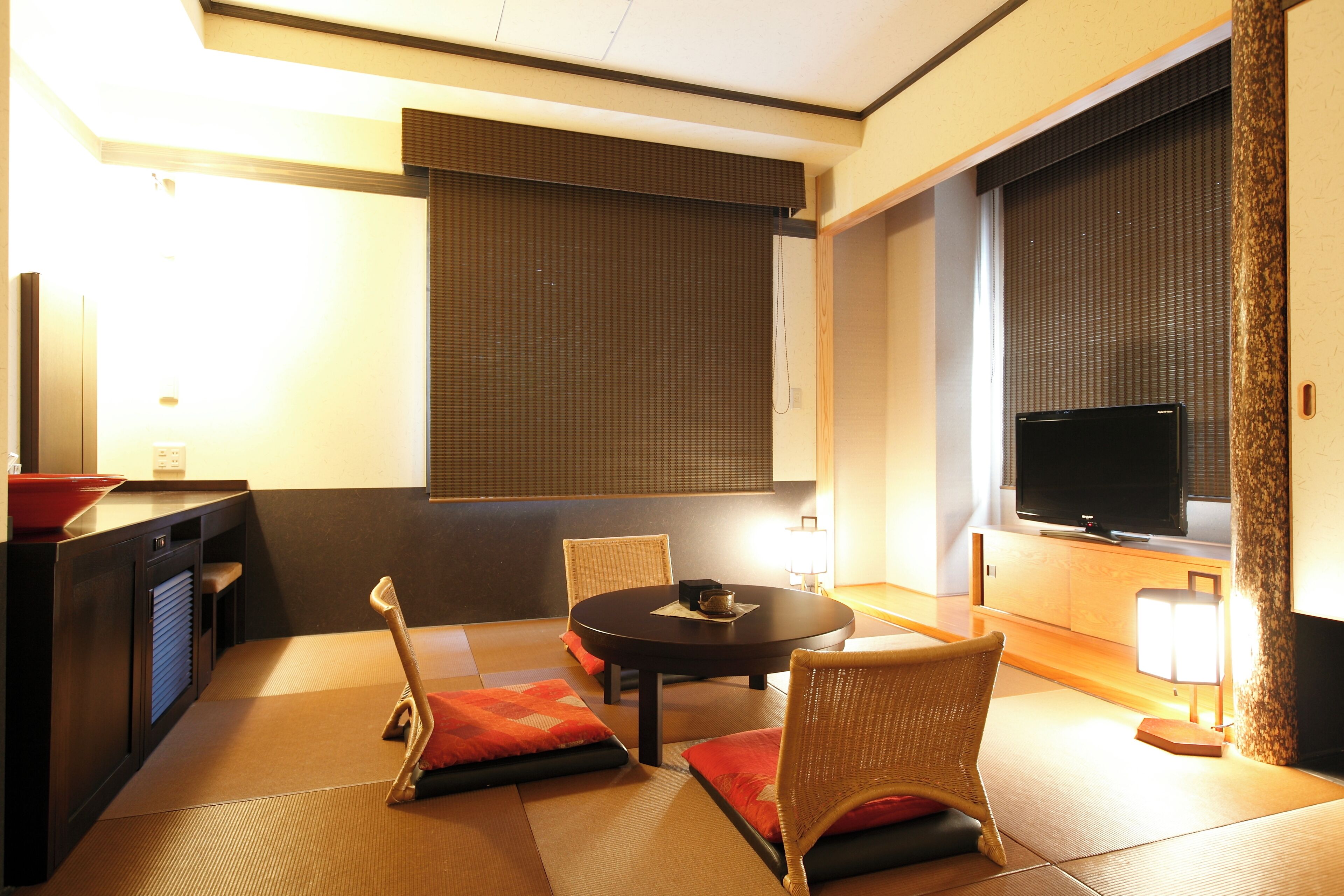 Ett modernt hotellrum med tatamimattor på golvet, ett runt bord och traditionella japanska stolar.