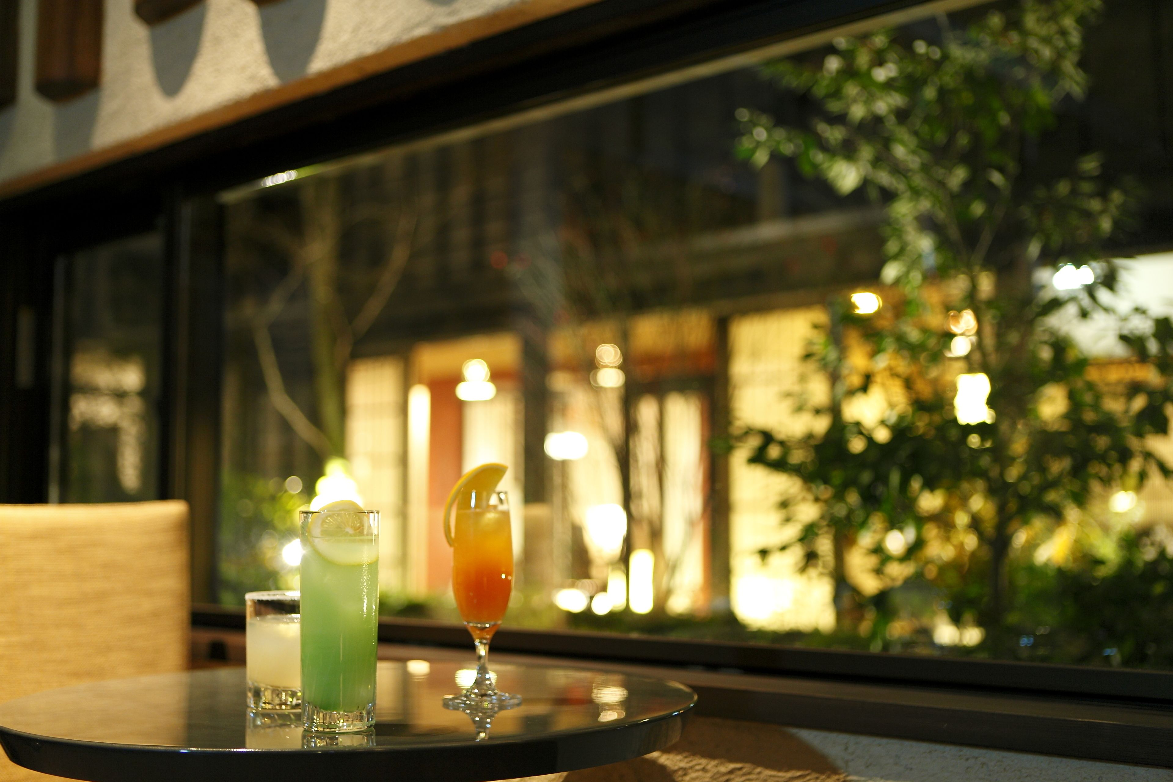 Une table avec deux verres contenant des boissons, dont l’un est garni d’une tranche de citron, et une vue par la fenêtre sur un bâtiment illuminé.