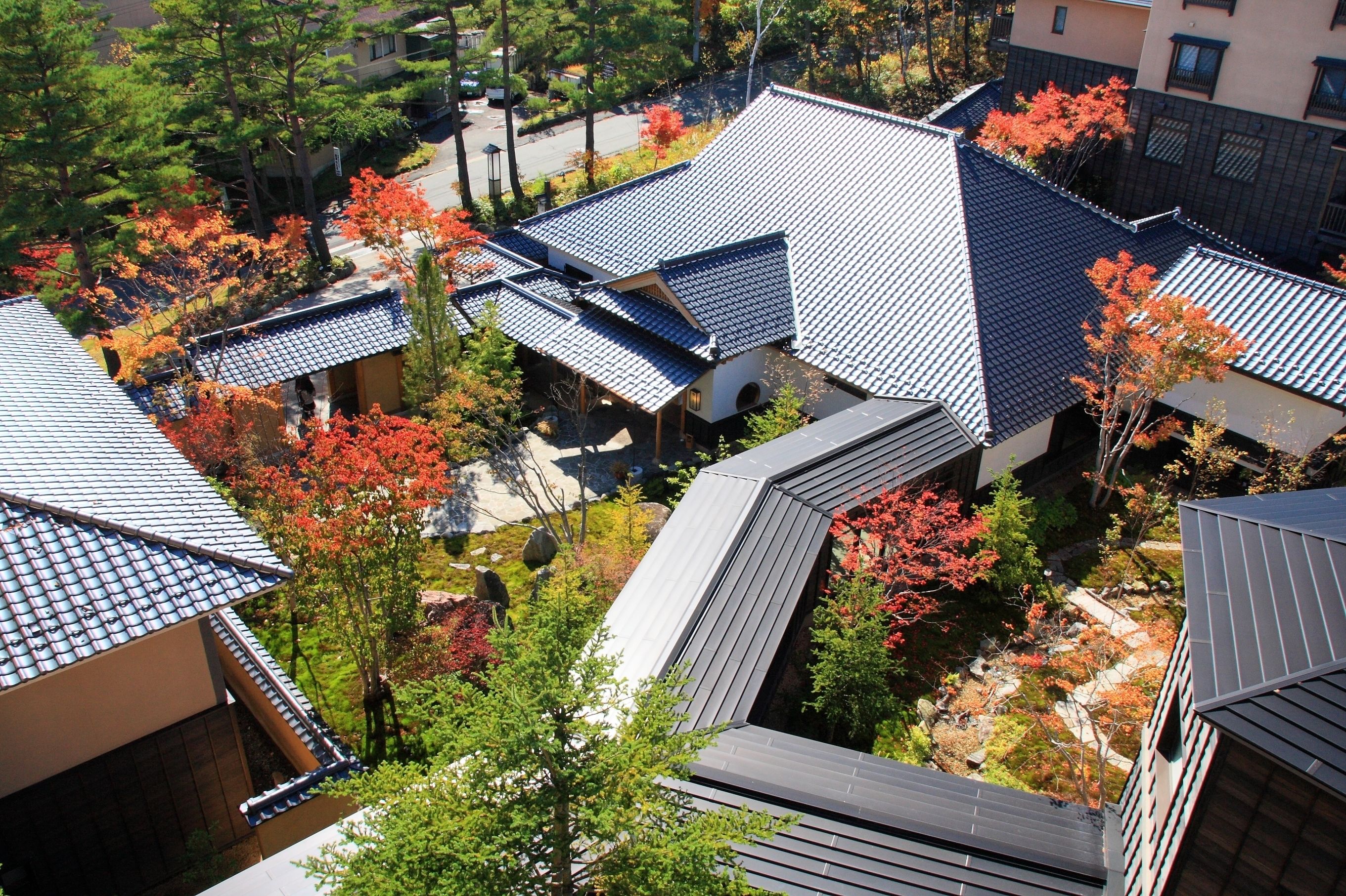 A residential area with traditional Japanese-style buildings, featuring sloped roofs and surrounded by autumn foliage.