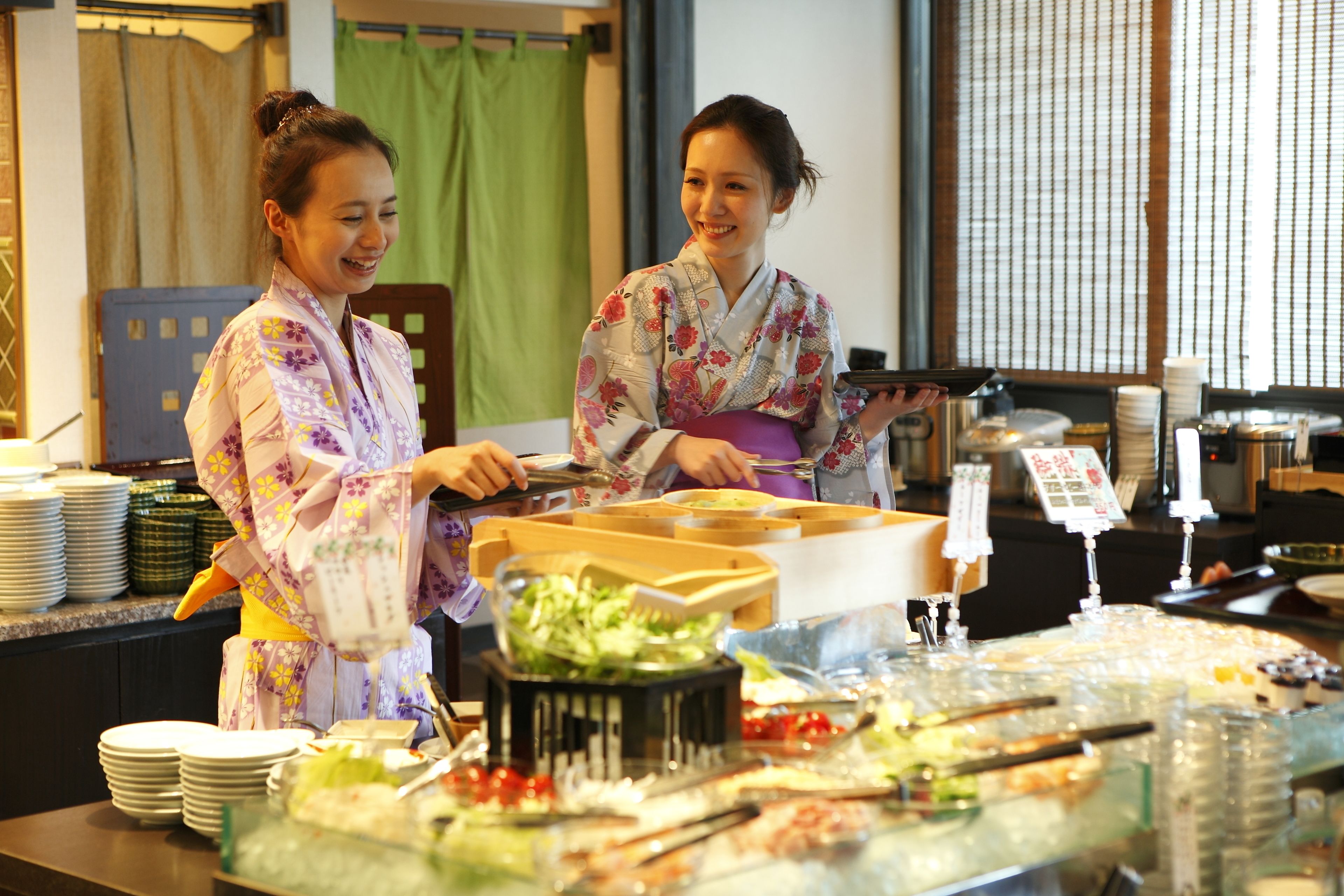 Two individuals in traditional attire serving food at a buffet with various dishes and condiments.