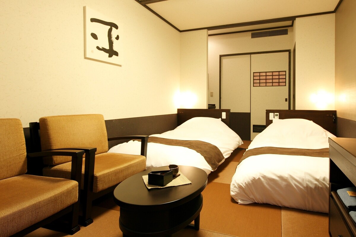A hotel room with two beds, a TV, a sofa, and a small table.