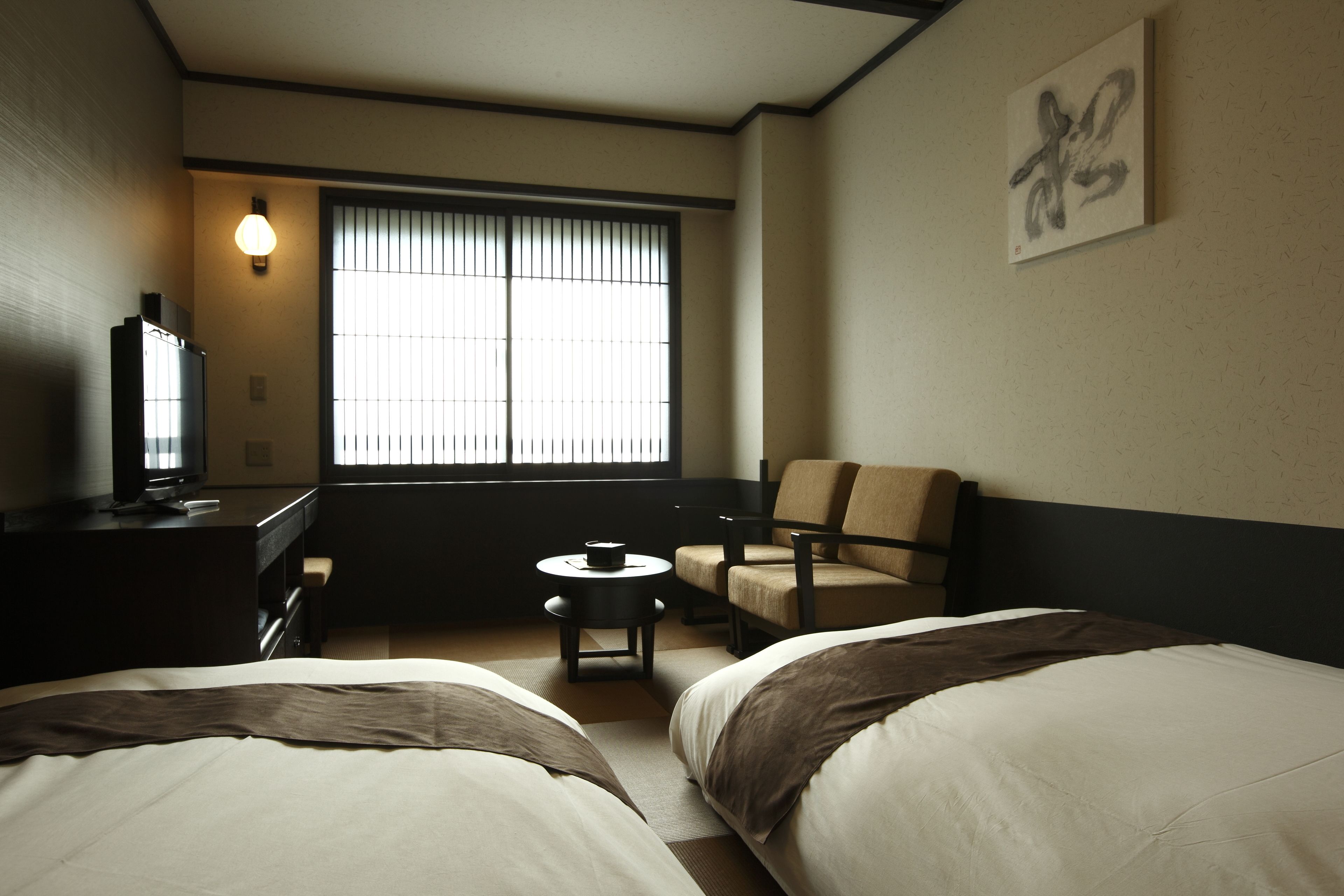 Une chambre d’hôtel avec deux lits, un bureau avec un ordinateur, une chaise, une petite table et une fenêtre avec des stores.
