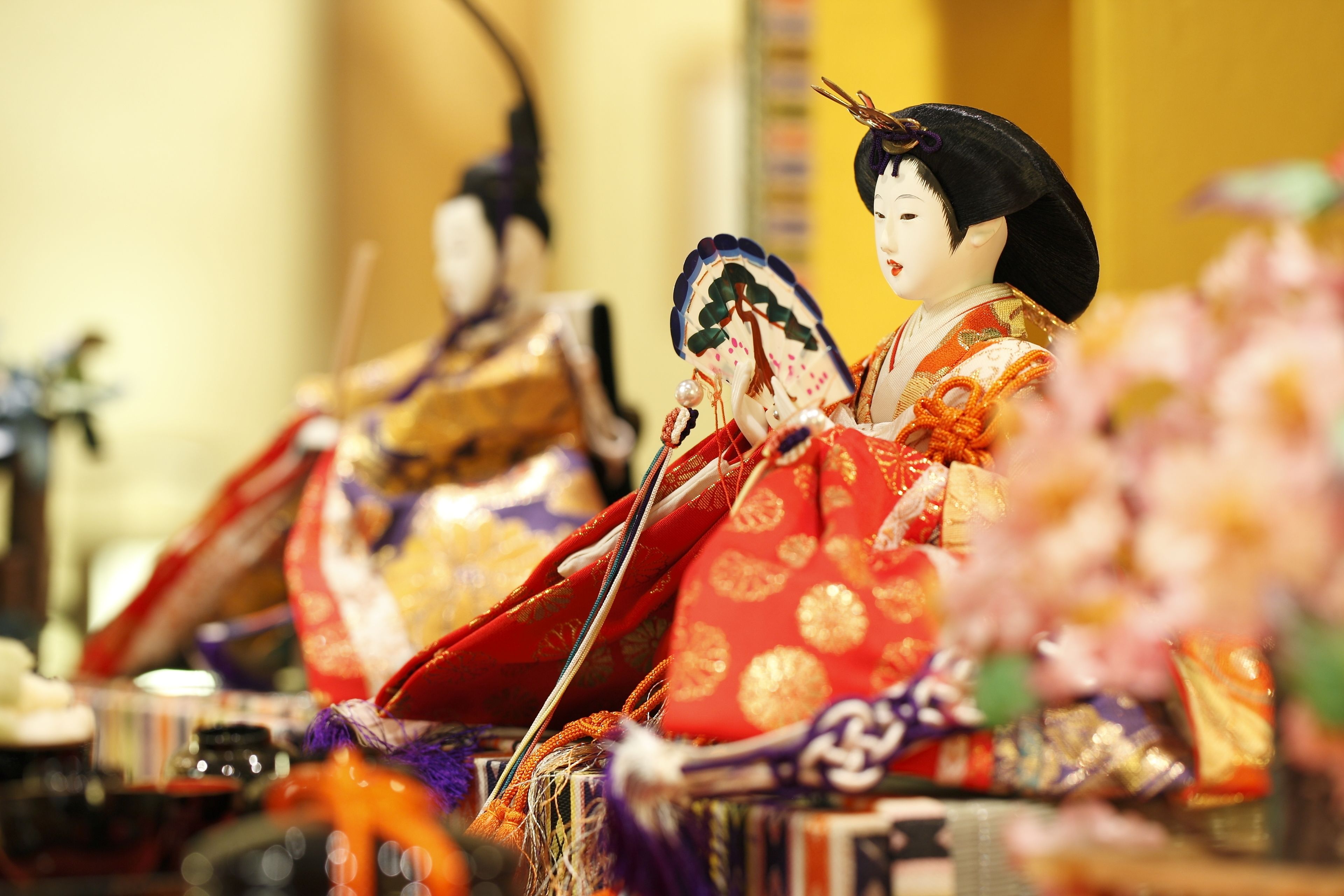 Una muñeca japonesa tradicional con vestimenta y accesorios detallados, sobre un fondo desenfocado.