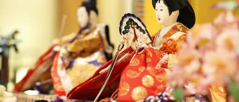 Una muñeca japonesa tradicional con vestimenta y accesorios detallados, sobre un fondo desenfocado.