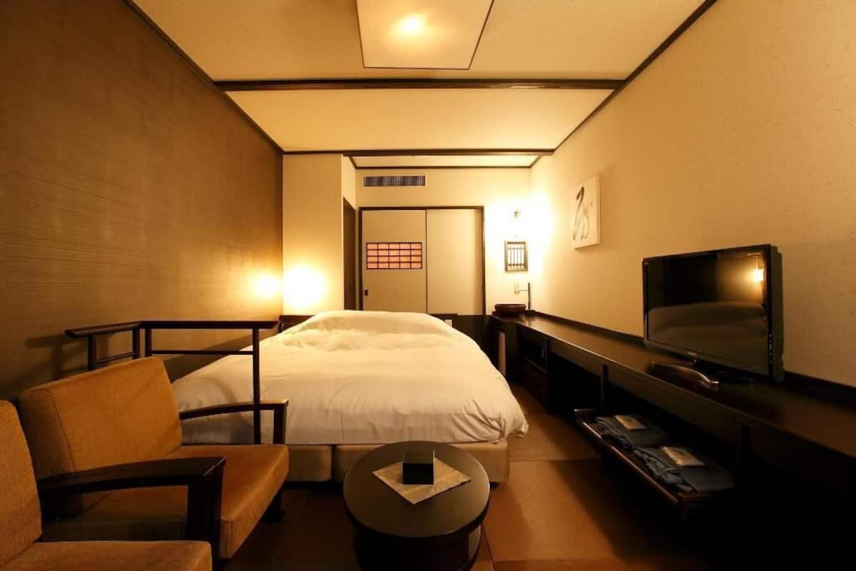 A hotel room with a bed, a TV, a desk, and a chair.