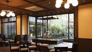 A restaurant with wooden furniture, large windows, and a view of greenery outside. - Oyado Konoha (Kusatsu)