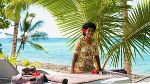A beachside massage setup with towels, a massage table, and a person in a floral shirt. - All inclusive Beachfront Villa in Fiji! (Sigatoka)