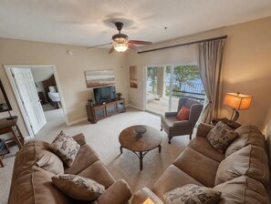 A living room with a sofa set, a coffee table, a ceiling fan, and a view of a balcony.