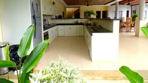 A spacious kitchen with white cabinets, a large island, and a dining area with wooden chairs. - Villa Mels (Jimbaran)