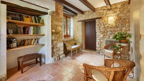 Un rincón acogedor para leer con pared de piedra, estanterías de madera, un banco, sillas de mimbre y una planta en maceta.