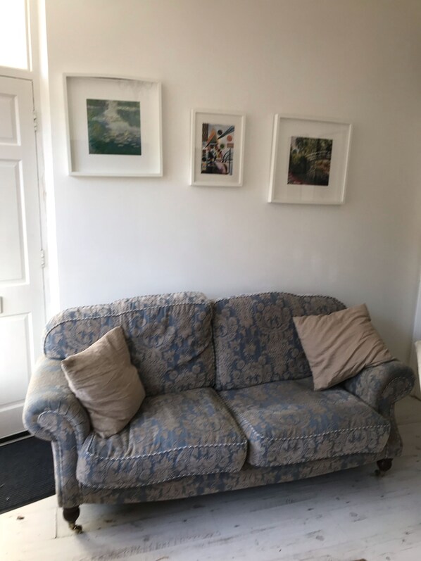 Un divano blu con motivi decorativi e due cuscini, una porta bianca e tre quadri appesi al muro.