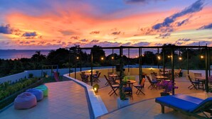 A rooftop terrace with outdoor seating, a pool, and a view of the sunset over the ocean. - The Happinezz Hills Hotel Karimunjawa (Karimun Jawa)